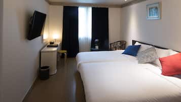 A hotel room with a bed, a desk, a chair, a TV, and a window with curtains.