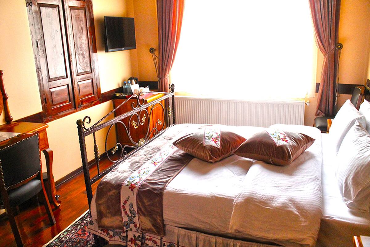 A bedroom with a wooden bed frame, a bedside table, a chair, and a window with curtains.