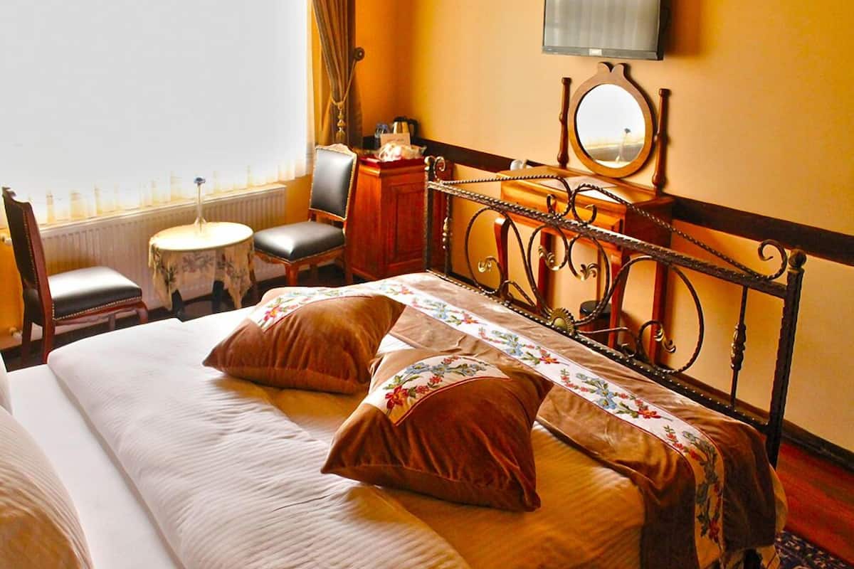 A hotel room with a bed, a desk, a chair, a small table, a mirror, and a TV.