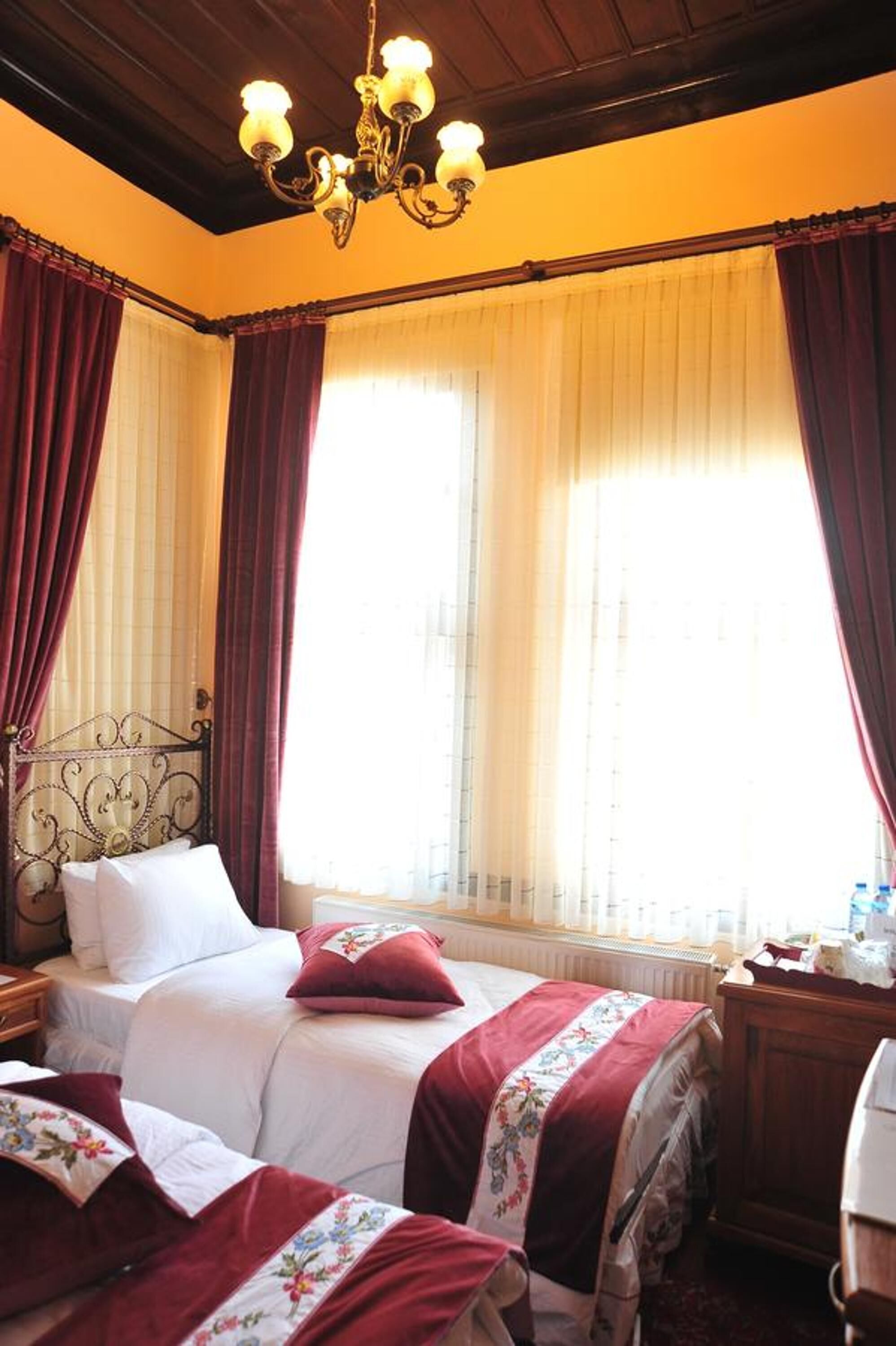 A room with a bed, a nightstand, a wooden dresser, and a chandelier.