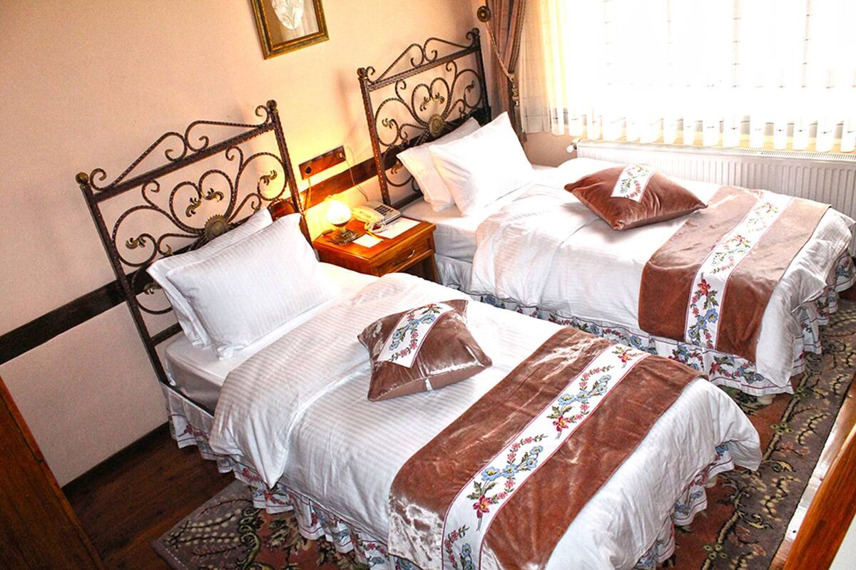 Two twin beds with headboards, a bedside table with a lamp, and a window with curtains.