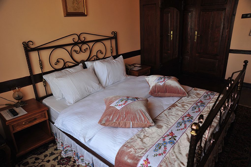 A neatly made bed with a floral-patterned bedspread, a wooden nightstand with a lamp, and a dark wooden headboard.