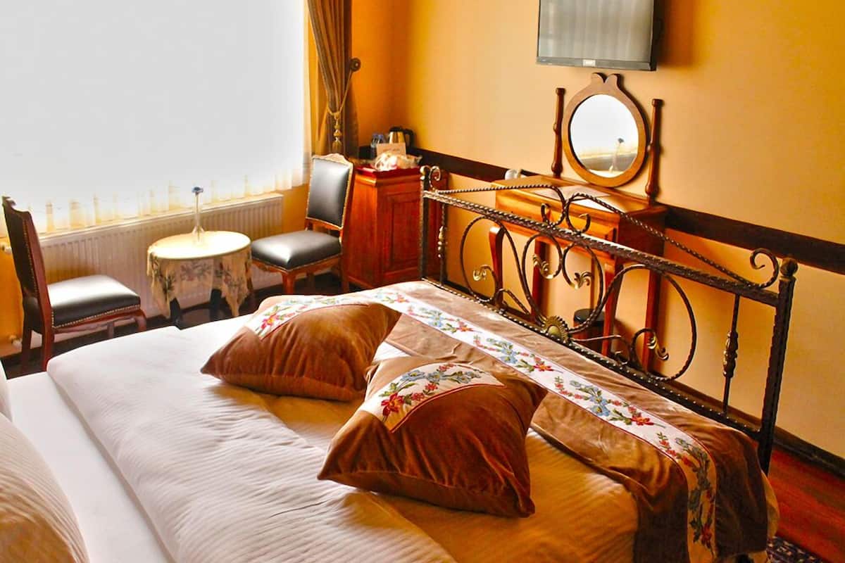 A hotel room with a large bed, a desk, a chair, a small table, a television, and a window with curtains.