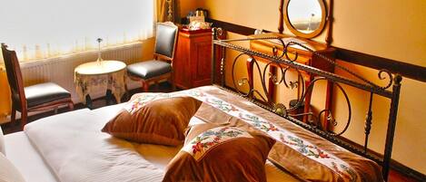 Una habitación de hotel con una cama grande, un escritorio, una silla, una mesita, un televisor y una ventana con cortinas.
