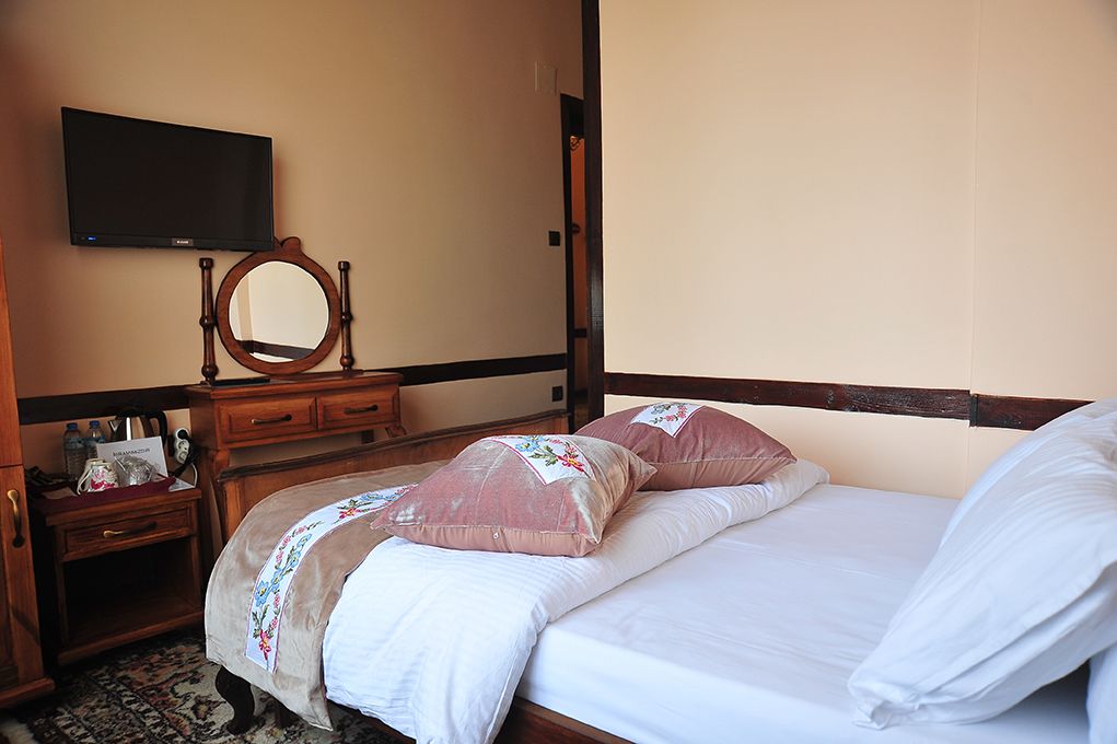 A bedroom with a bed, pillows, a dresser, a mirror, and a television on the wall.