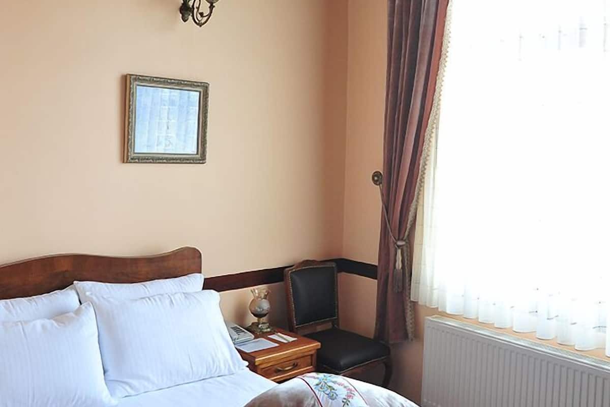 A bedroom with a bed, a nightstand, a lamp, a framed picture, and a window with curtains.