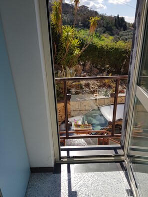 Un balcon donnant sur un jardin aménagé, un mur de pierre et un bâtiment situé au loin.