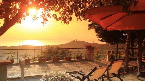 A terrace with a view of the sunset over the sea, potted plants, and a red umbrella. - B&B Il Giardino Di Armida (Ogliastro Cilento)