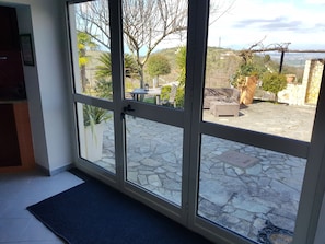 Une pièce dotée d’une grande porte vitrée donnant sur un patio extérieur avec un sol en pierre, une table et un canapé.
