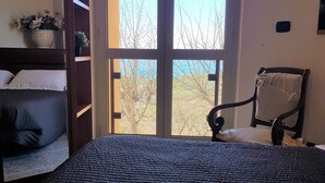 A bedroom with a large bed, a chair, a window with a view of trees, and a small table with a plant. - B&B Il Giardino Di Armida (Ogliastro Cilento)