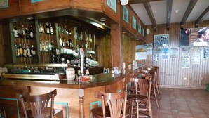 Zona de bar con mostrador de madera, taburetes y estantes llenos de botellas.
