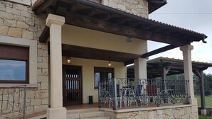 Un edificio de piedra con un porche cubierto, escalones que conducen a la entrada y mobiliario para estar al aire libre.