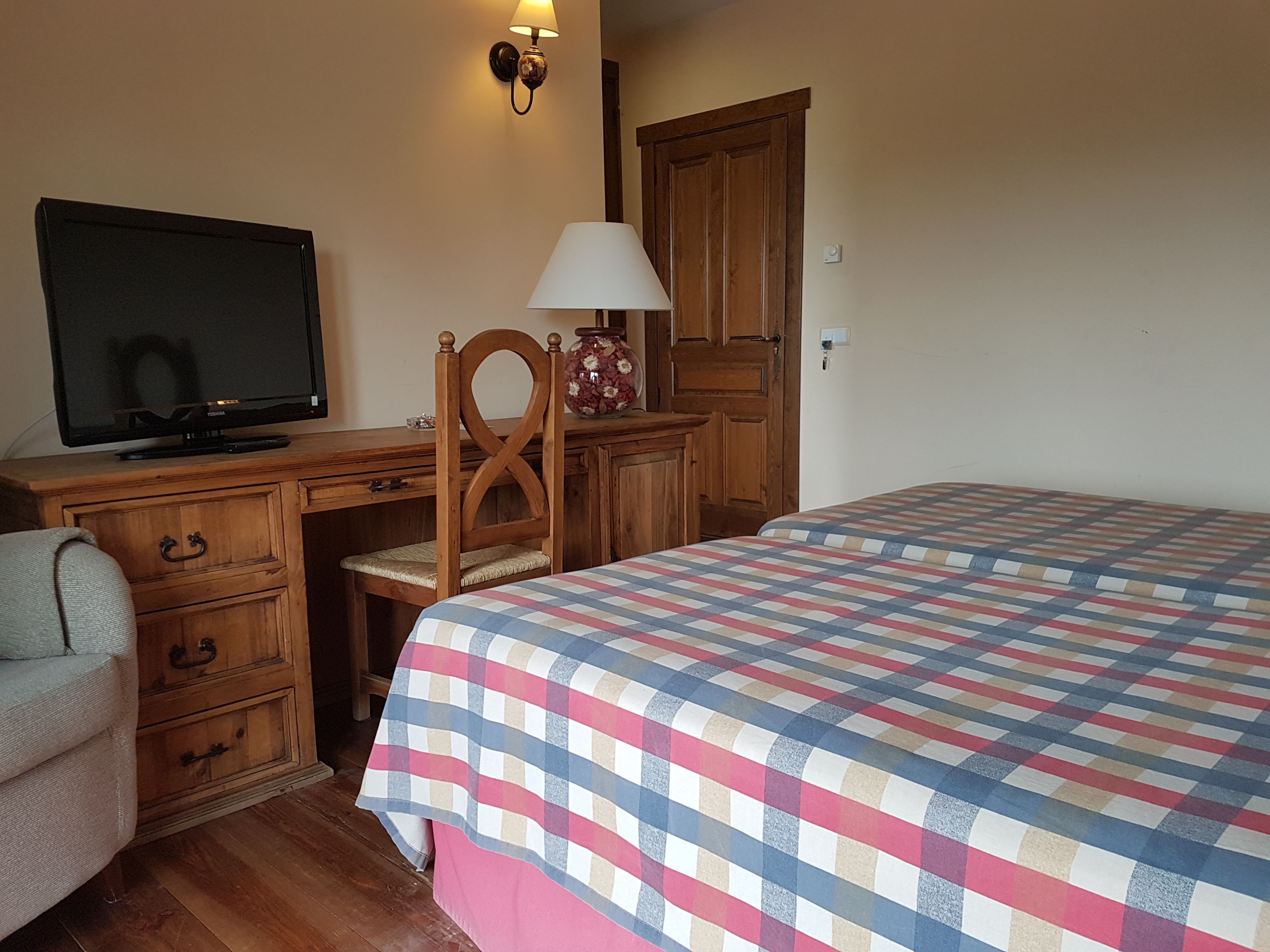 A bedroom with a bed, a desk with a television, a chair, and a lamp.