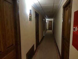 A long, narrow hallway with wooden doors on both sides, a radiator on the left, and a red bulletin board on the right. - Hotel Garabatos (Navarredonda de Gredos)