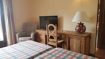 A room with two beds, a desk, a chair, a television, and a lamp.