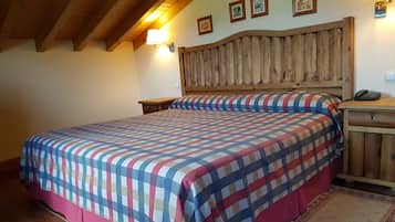 Un dormitorio con cabecera de madera, colcha a cuadros, mesita de noche con lámpara y teléfono.