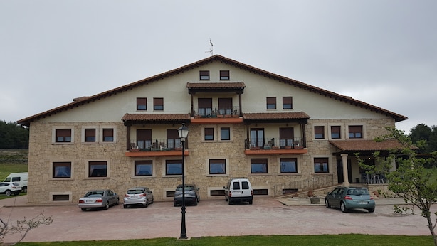 Un edificio de varios pisos con balcones, una zona de estacionamiento y un primer plano con césped.