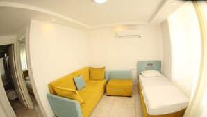 A compact room with a yellow sofa, a matching ottoman, and a single bed with a white mattress. - Queenaba Beach (Erdemli)