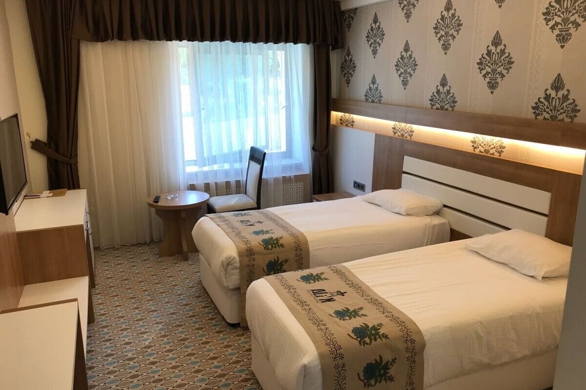 A hotel room with two beds, a desk, a chair, and a television.