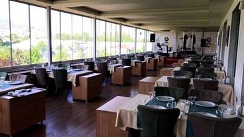 Un restaurante con varias mesas y sillas, ventanas amplias y vista al exterior.