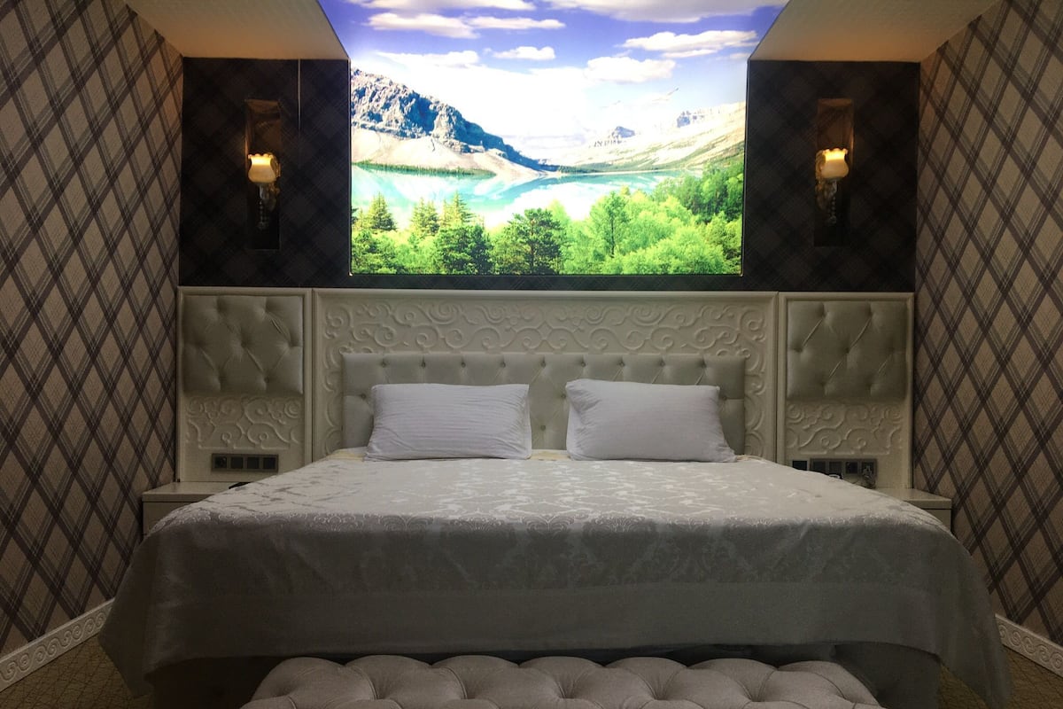 A bedroom with a large bed, two wall sconces, a window with a mountain view, and a tufted bench.