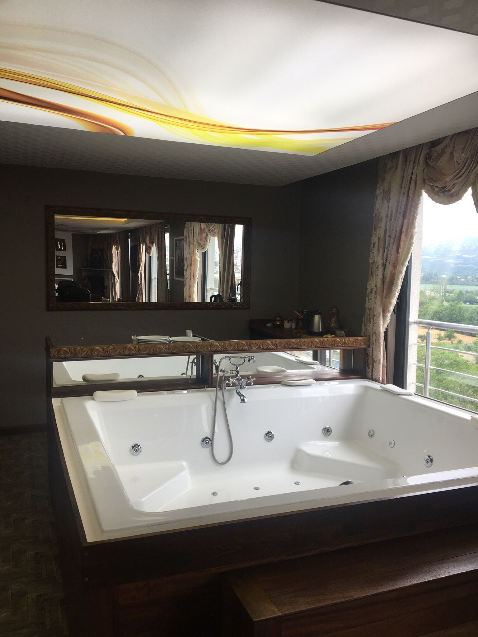 A bathroom with a large bathtub, a mirror, and a view of greenery outside.