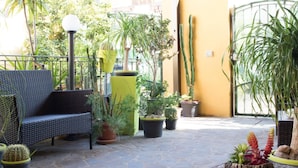 An outdoor patio with a wicker sofa, various potted plants, a cactus, and a wooden stump with flowers. - Affittacamere Al Mare (Oristano)