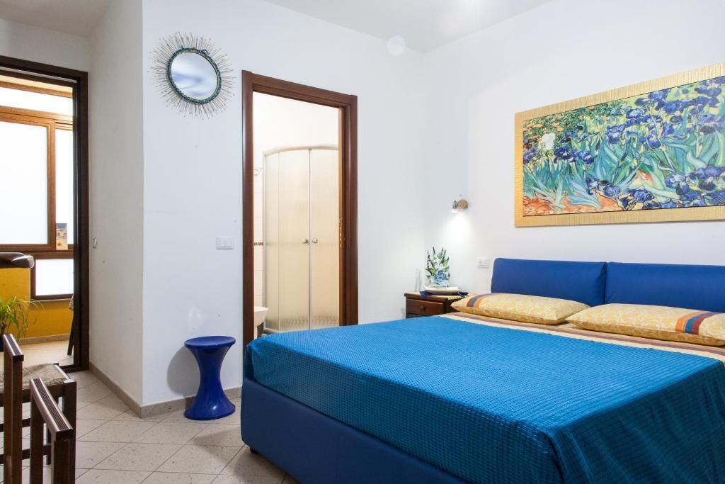 A bedroom with a large bed, a blue accent wall, a painting, and a door leading to another room.