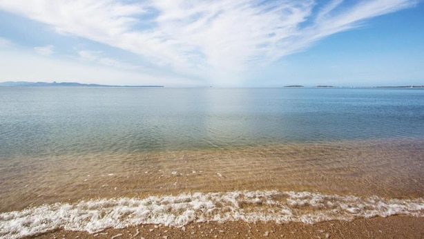 A beach with clear water, gentle waves, and a distant shoreline. - Affittacamere Al Mare (Oristano)