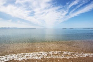 A beach with clear water, gentle waves, and a distant shoreline. - Affittacamere Al Mare (Oristano)