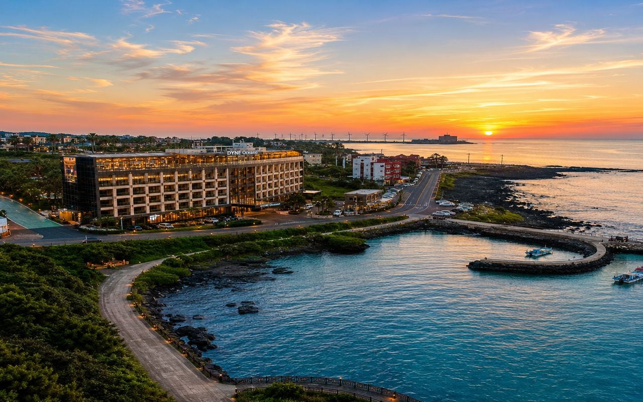 A coastal hotel with a marina, a road leading to the property, and a sunset in the background.