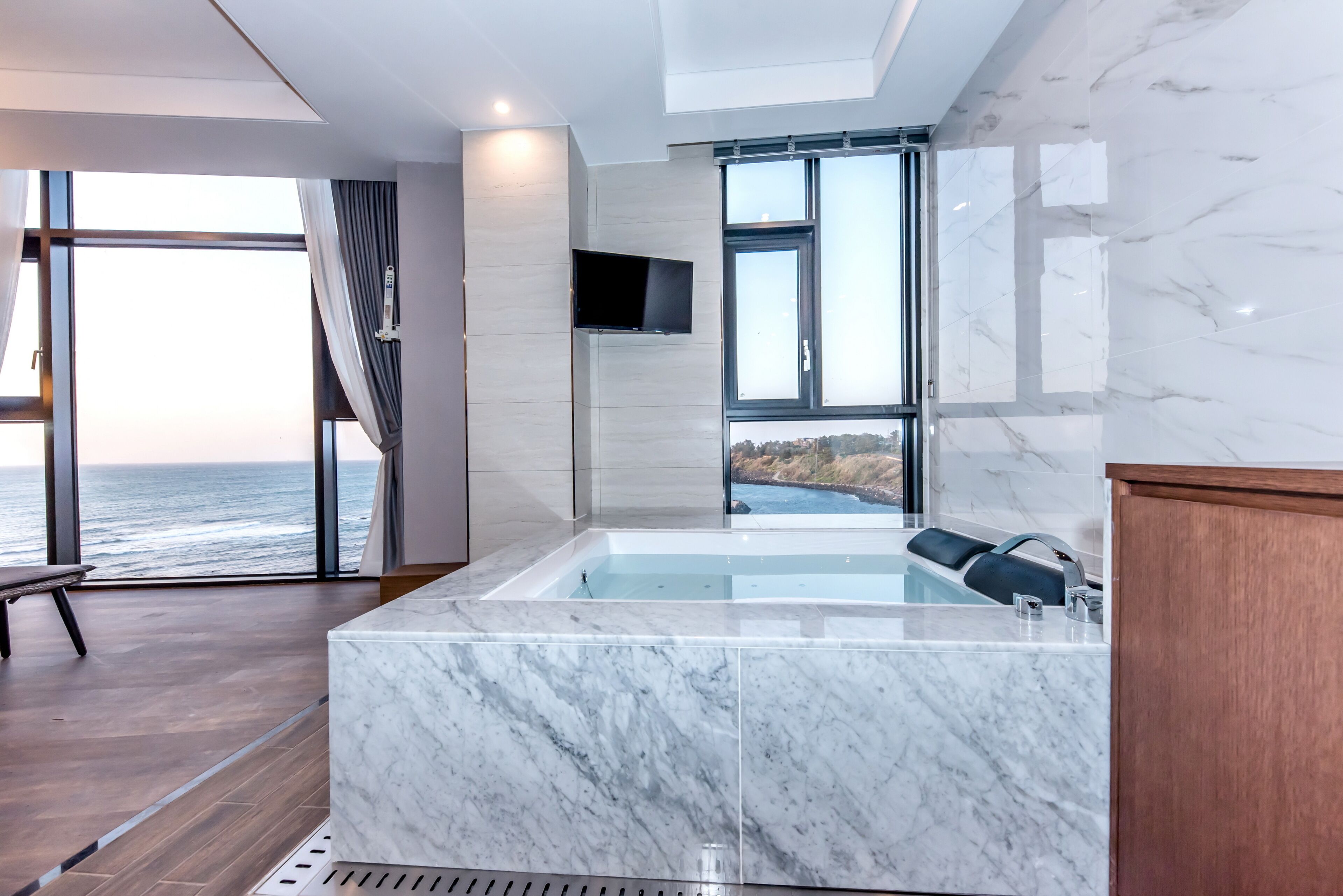 A modern bathroom with a large bathtub, a TV mounted on the wall, and a view of the ocean.