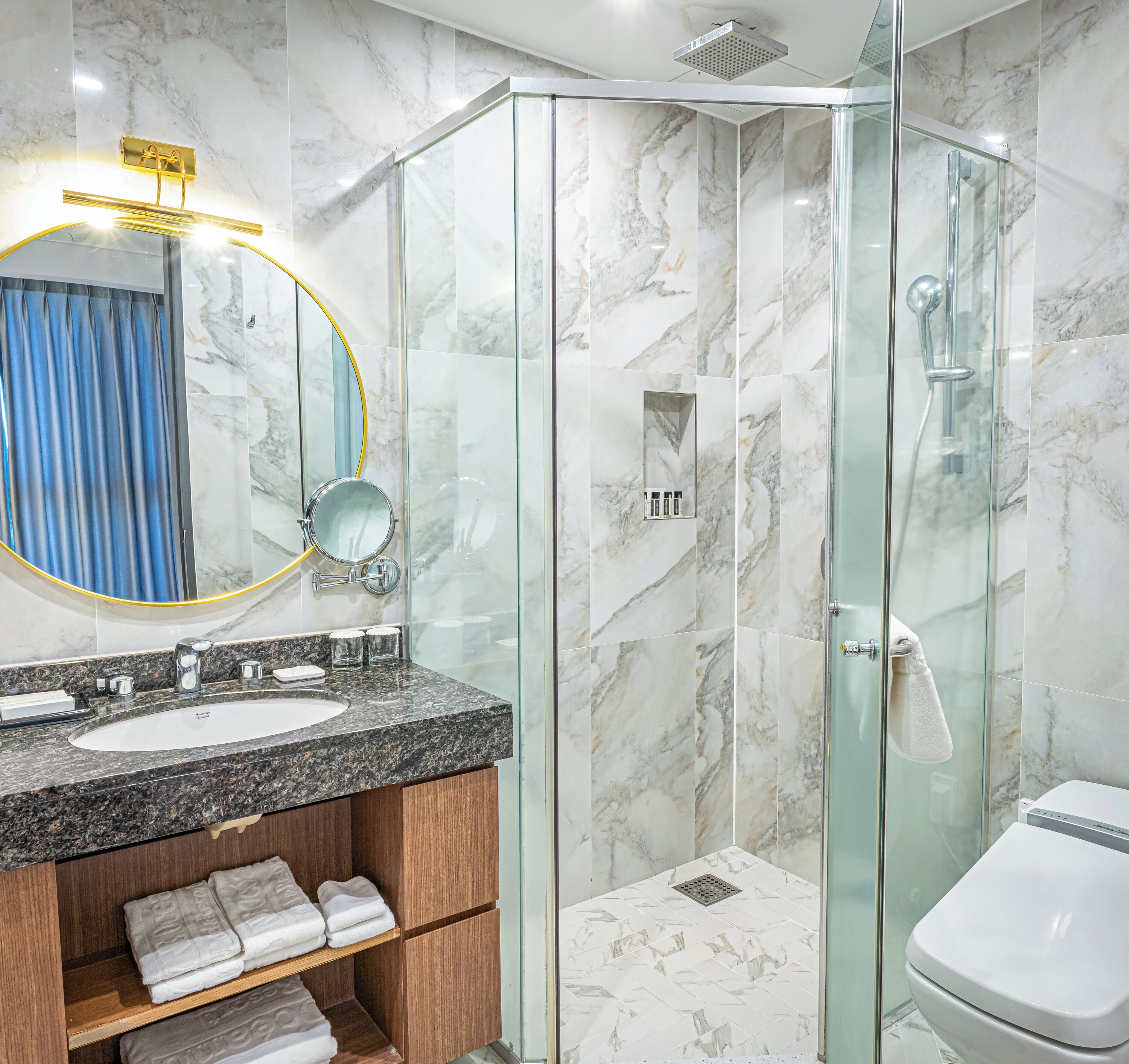 A modern bathroom with a glass-enclosed shower, a marble-tiled wall, a sink with a granite countertop, and a mirror with a gold frame.