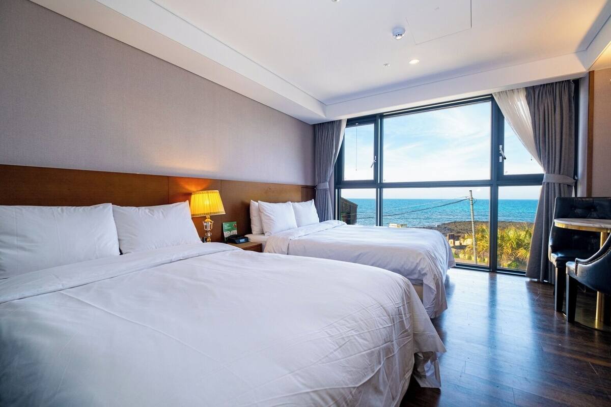 Une chambre d’hôtel avec deux lits, un bureau et une grande fenêtre donnant sur la mer.