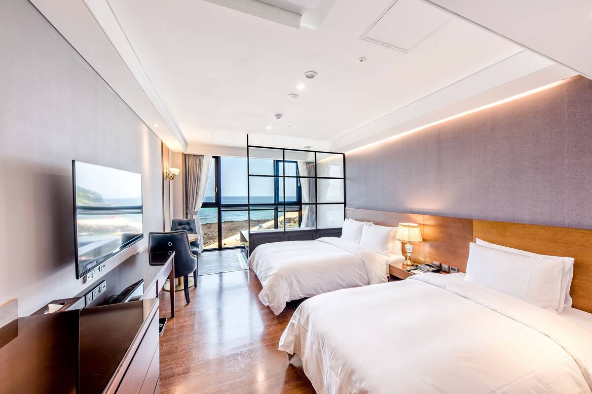 Une chambre d’hôtel avec deux lits, une télévision, un bureau et une vue sur la plage.