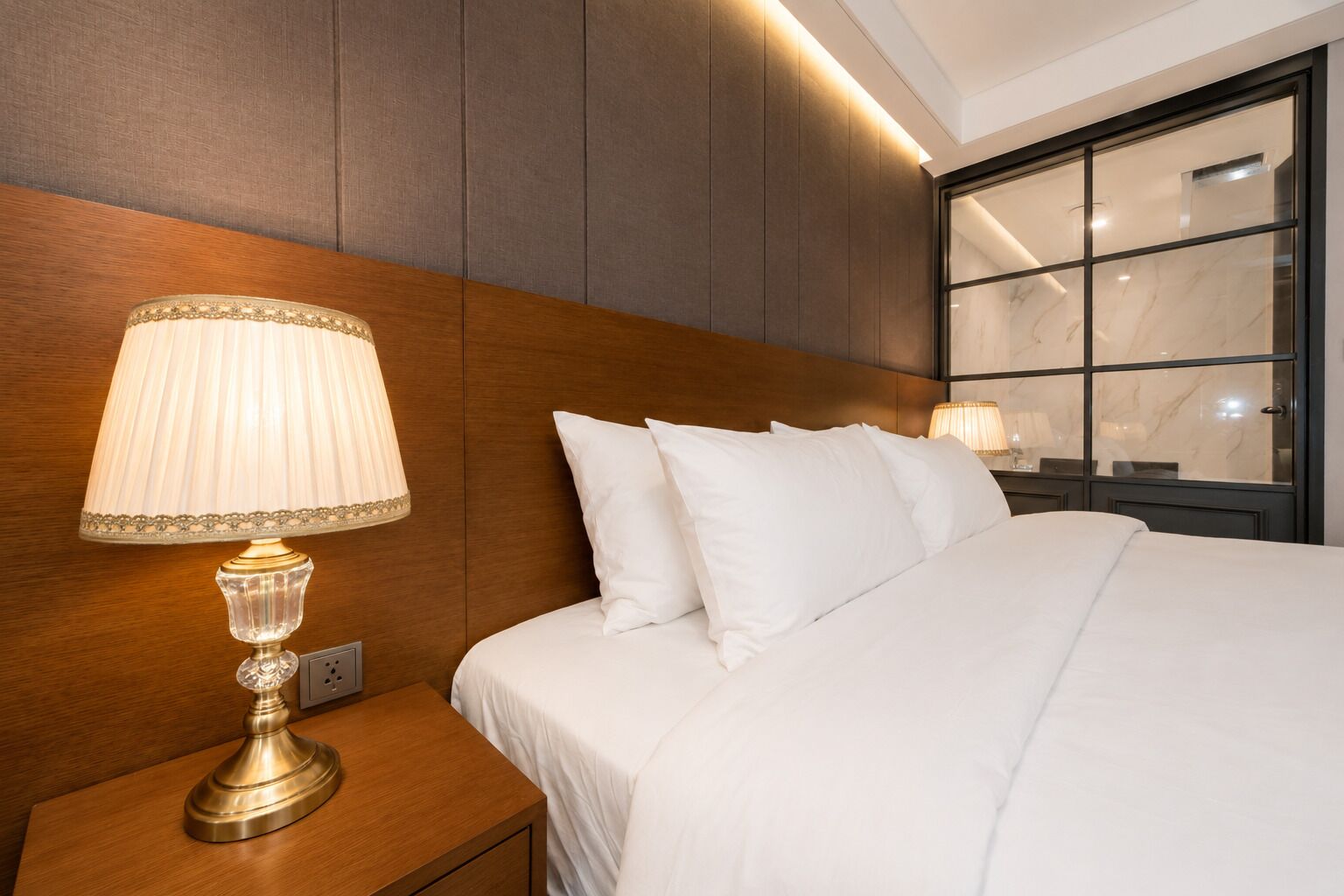 A hotel room with a bed, a nightstand with a lamp, and a window with a view.