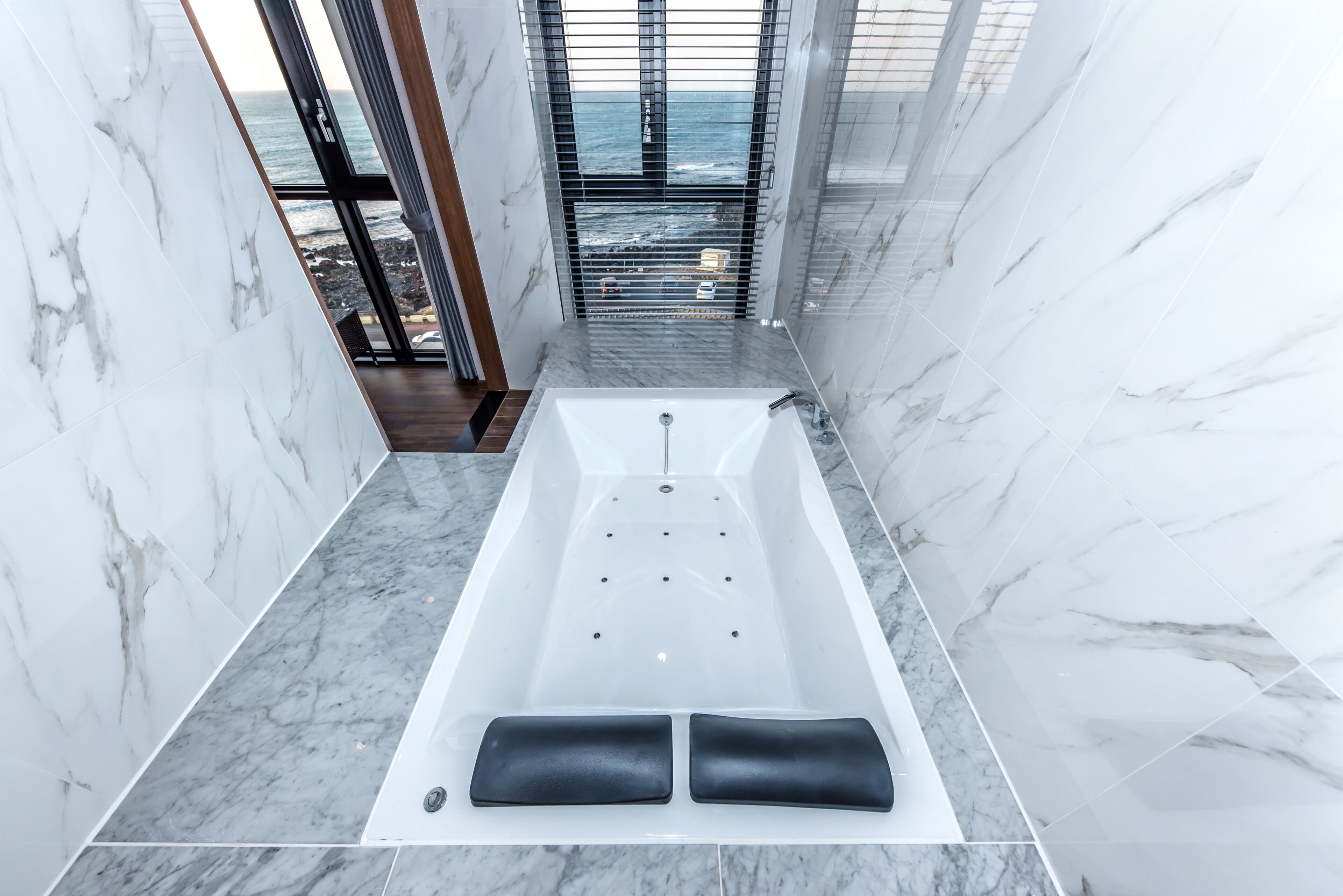 Une salle de bain moderne avec une grande baignoire, des murs en marbre et une vue sur l’océan.