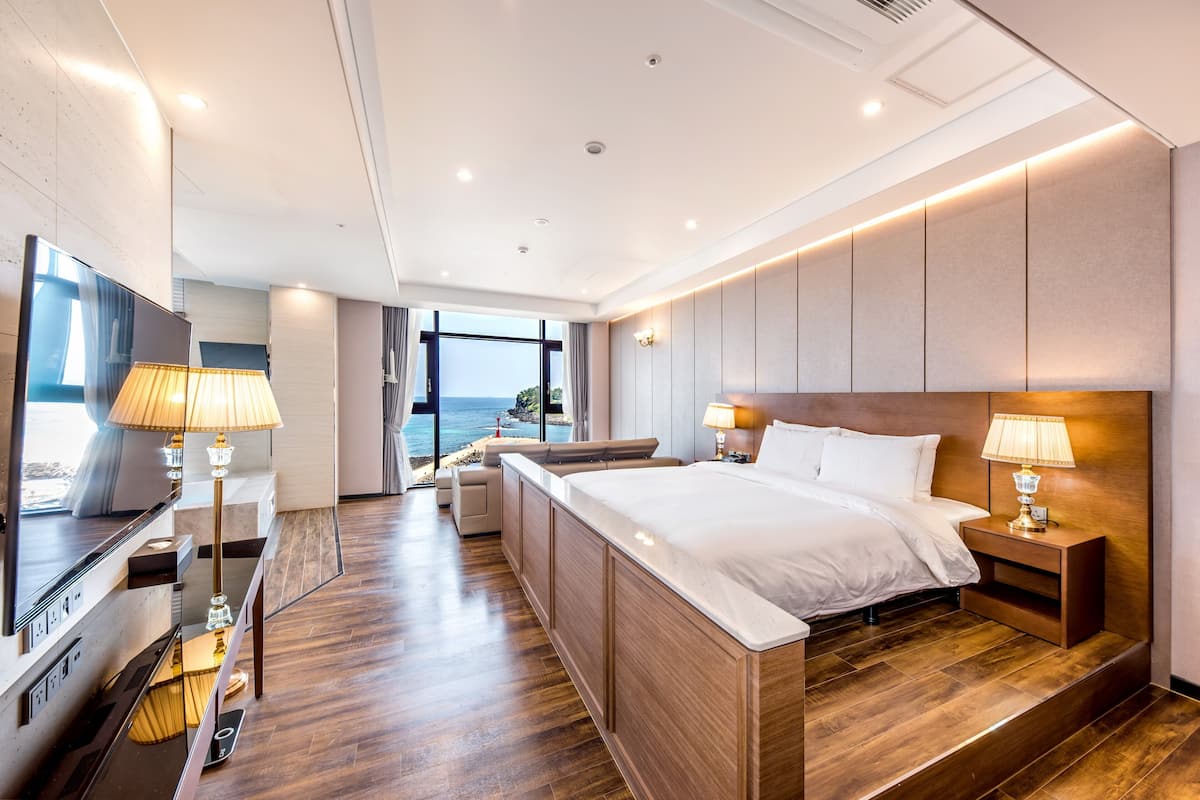 Une chambre d’hôtel moderne avec un grand lit, des lampes de chevet, une télévision et une vue sur la mer.