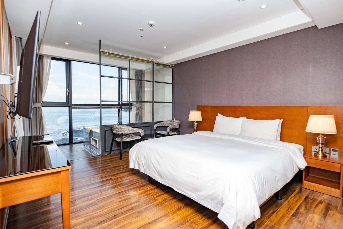 Une chambre d’hôtel moderne dotée d’un grand lit, d’un bureau et offrant une vue sur l’océan.