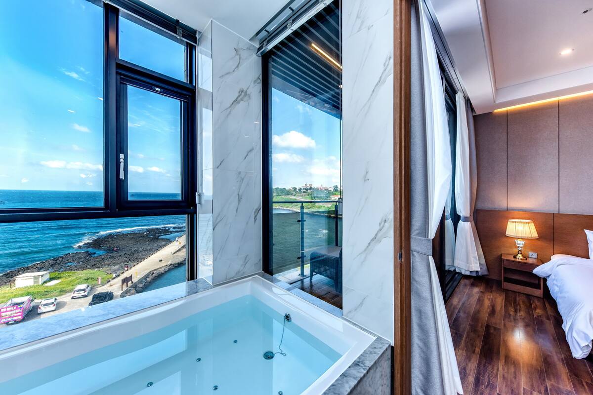 Une chambre dotée d’une grande baignoire, d’un lit, d’une table de chevet et offrant une vue sur l’océan.