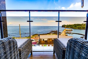 Un balcón con sillas de mimbre y vistas al mar y la costa.