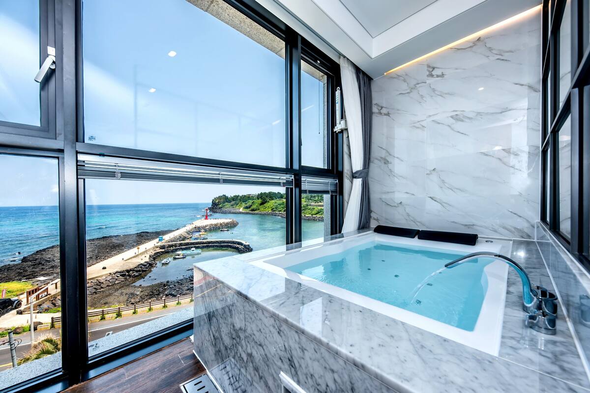 Une salle de bain moderne avec une grande baignoire, une vue sur la mer et un mur en marbre.