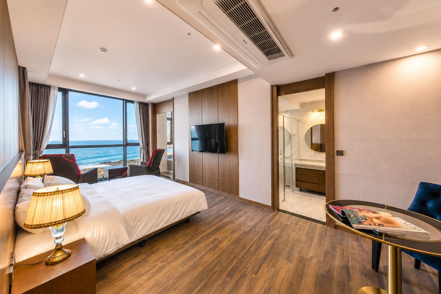Ein Hotelzimmer mit einem großen Bett, einem Schreibtisch mit Lampe, einem Fernseher und Blick aufs Meer.