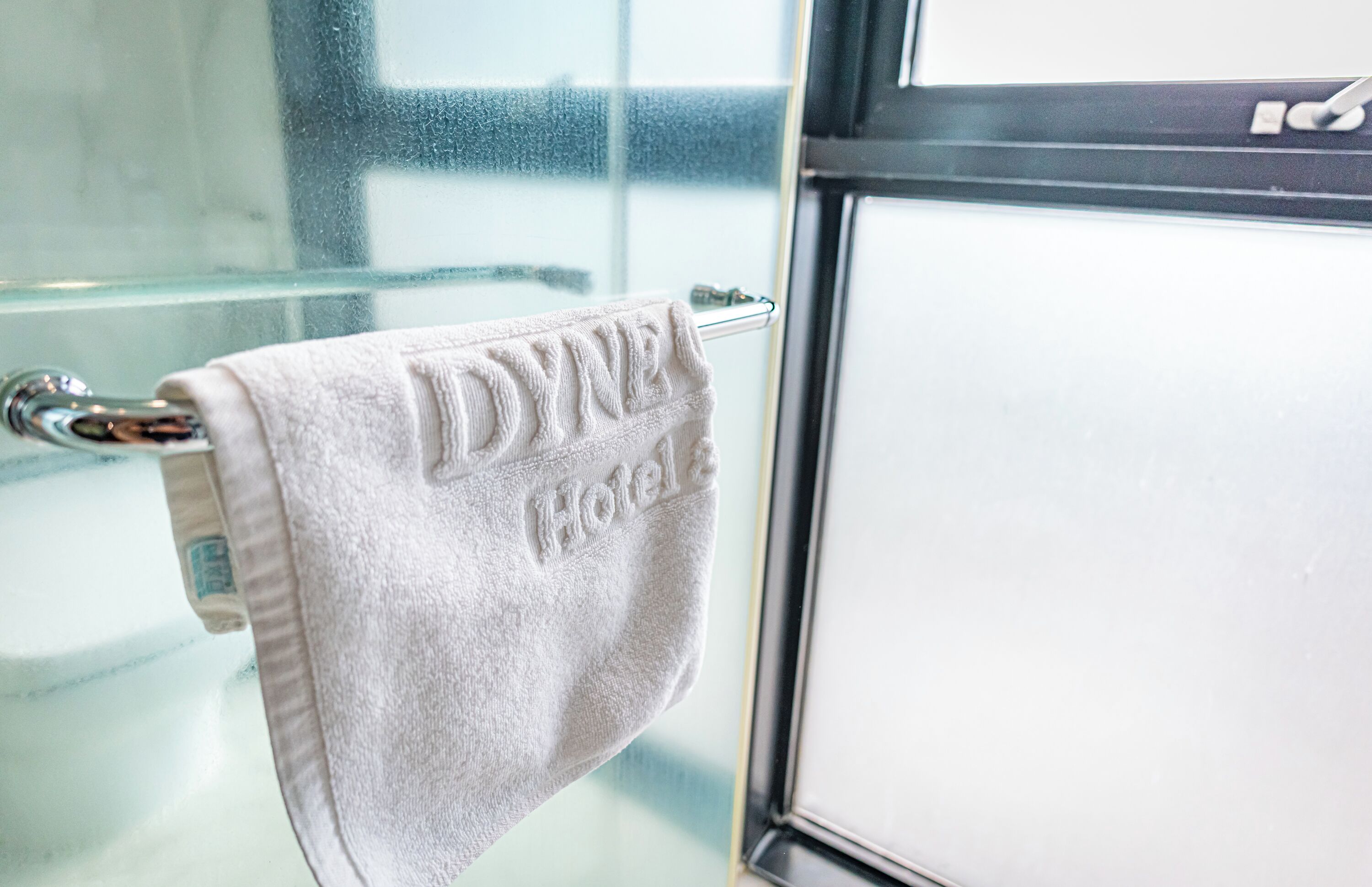 Ein Hotelhandtuch hängt an einer Glastür mit einem Milchglasfenster im Hintergrund.