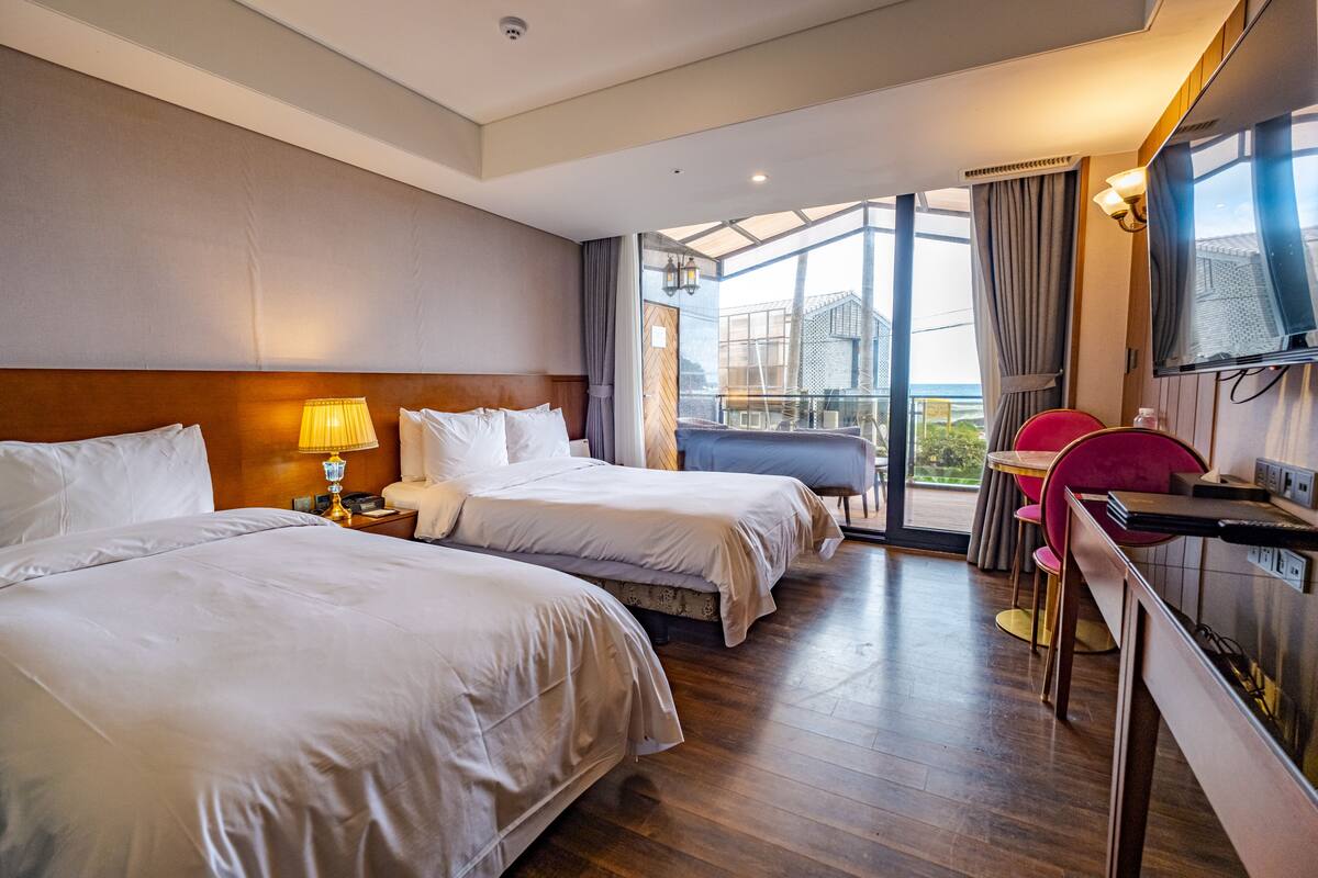 Une chambre d’hôtel avec deux lits, un bureau avec une chaise, une télévision et un balcon avec vue.