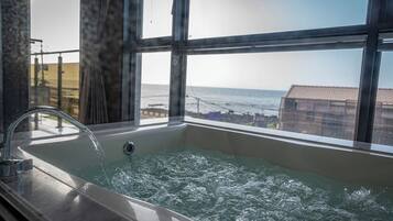 A bathtub with running water, large windows, and a view of the ocean.