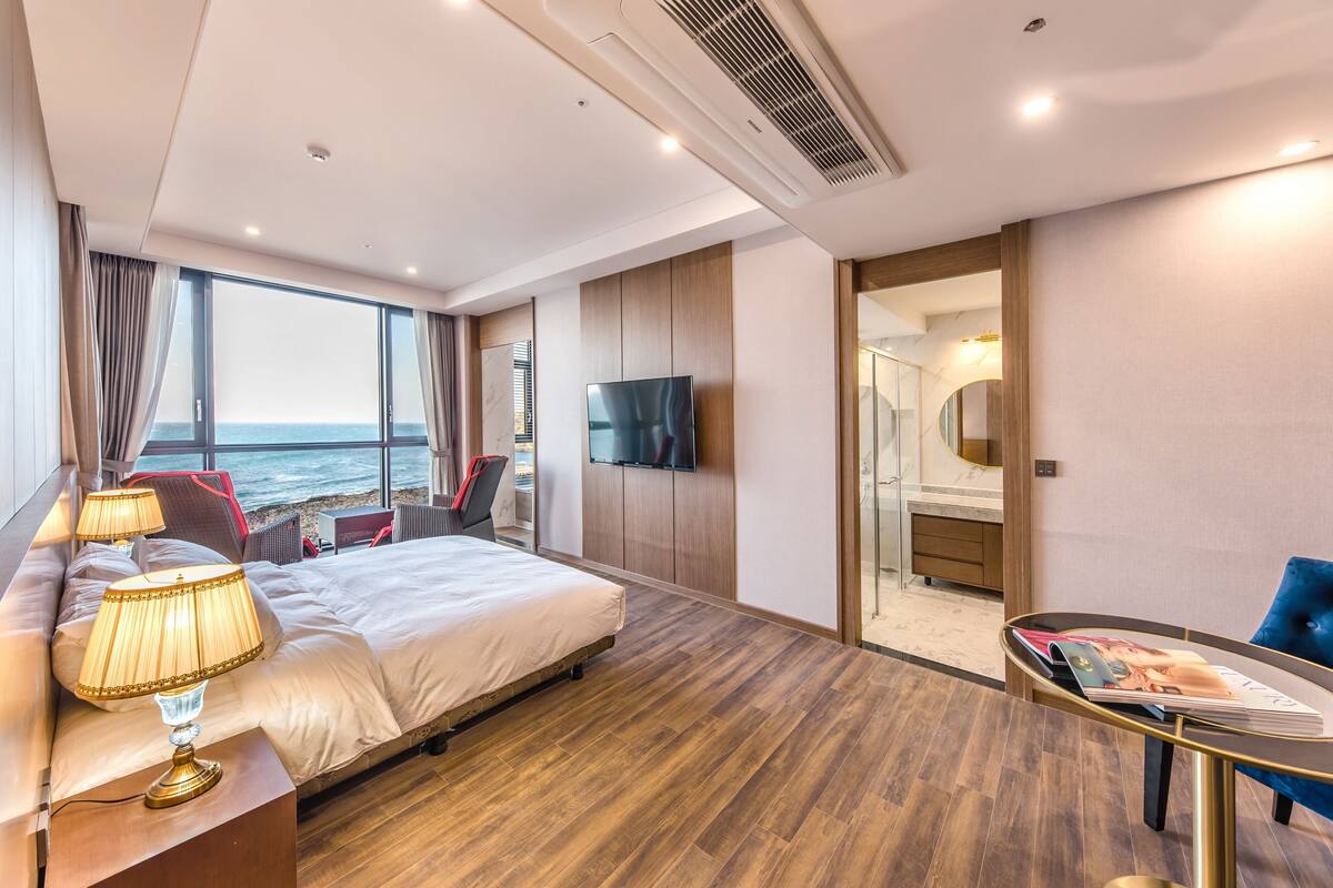 Une chambre d’hôtel moderne dotée d’un grand lit, d’une télévision, d’un bureau avec une chaise et offrant une vue sur la mer.