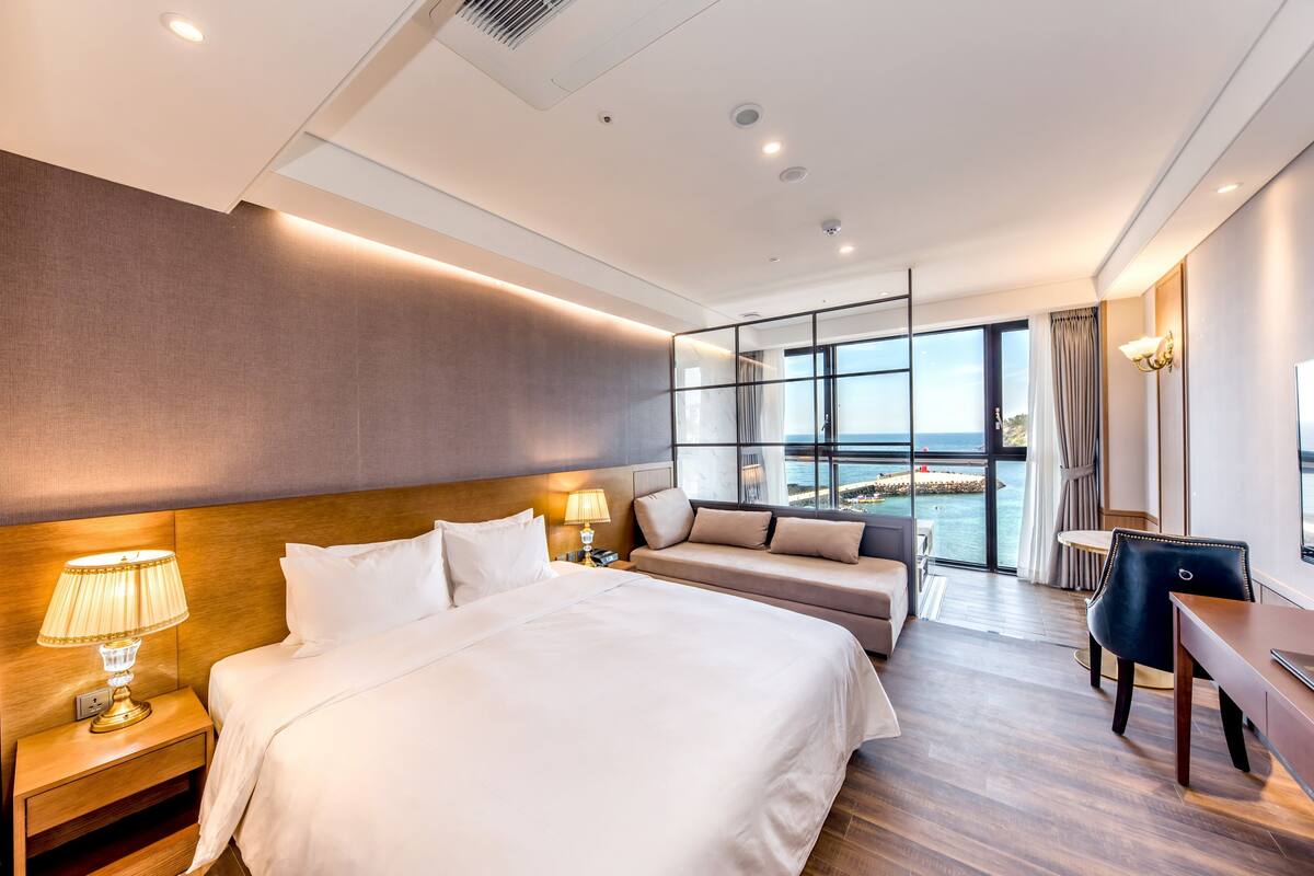 Une chambre d’hôtel moderne, dotée d’un grand lit, d’un canapé, d’un bureau et offrant une vue sur la mer.
