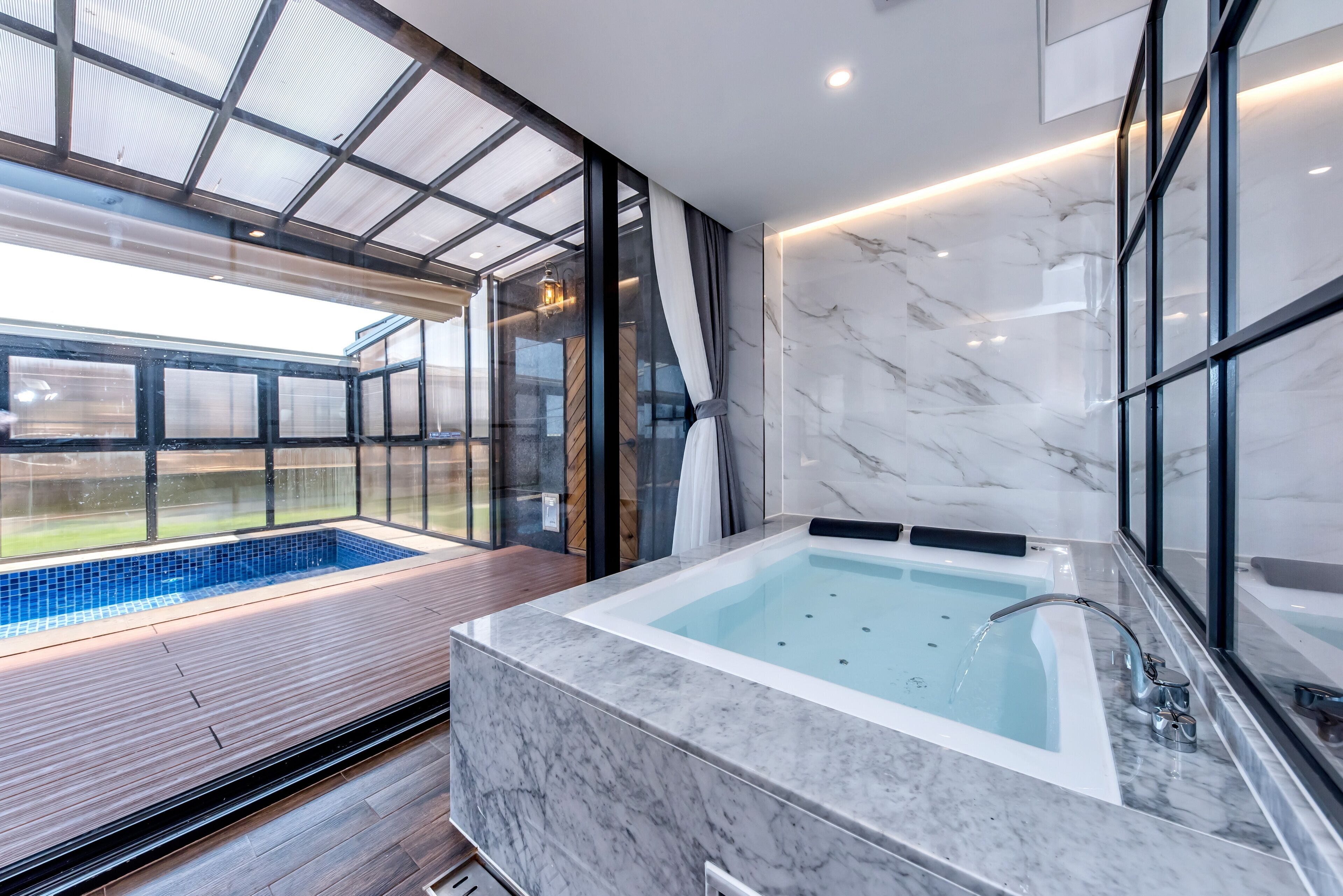 A modern bathroom with a marble sink, a bathtub, and a glass-enclosed pool area.