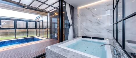 A modern bathroom with a marble sink, a bathtub, and a glass-enclosed pool area.